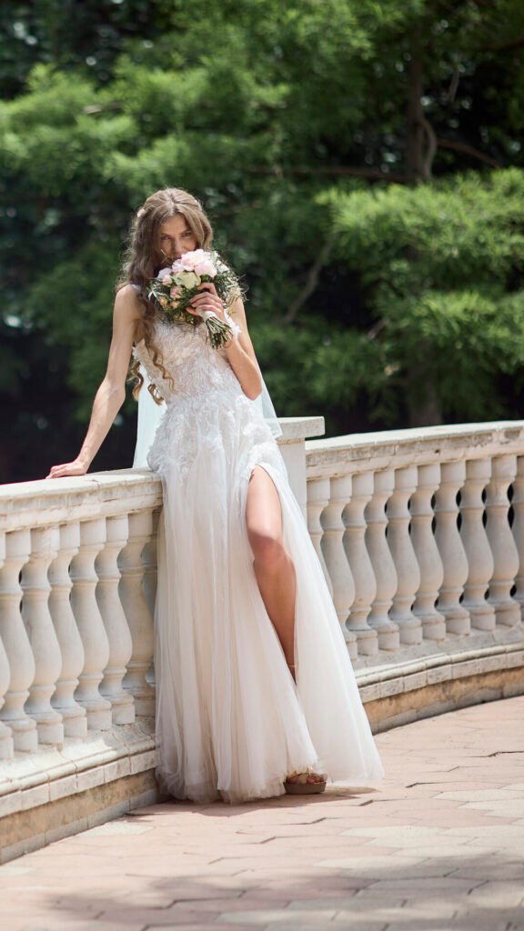 Bride wearing lace wedding dress with bouquet and long veil on a balcony