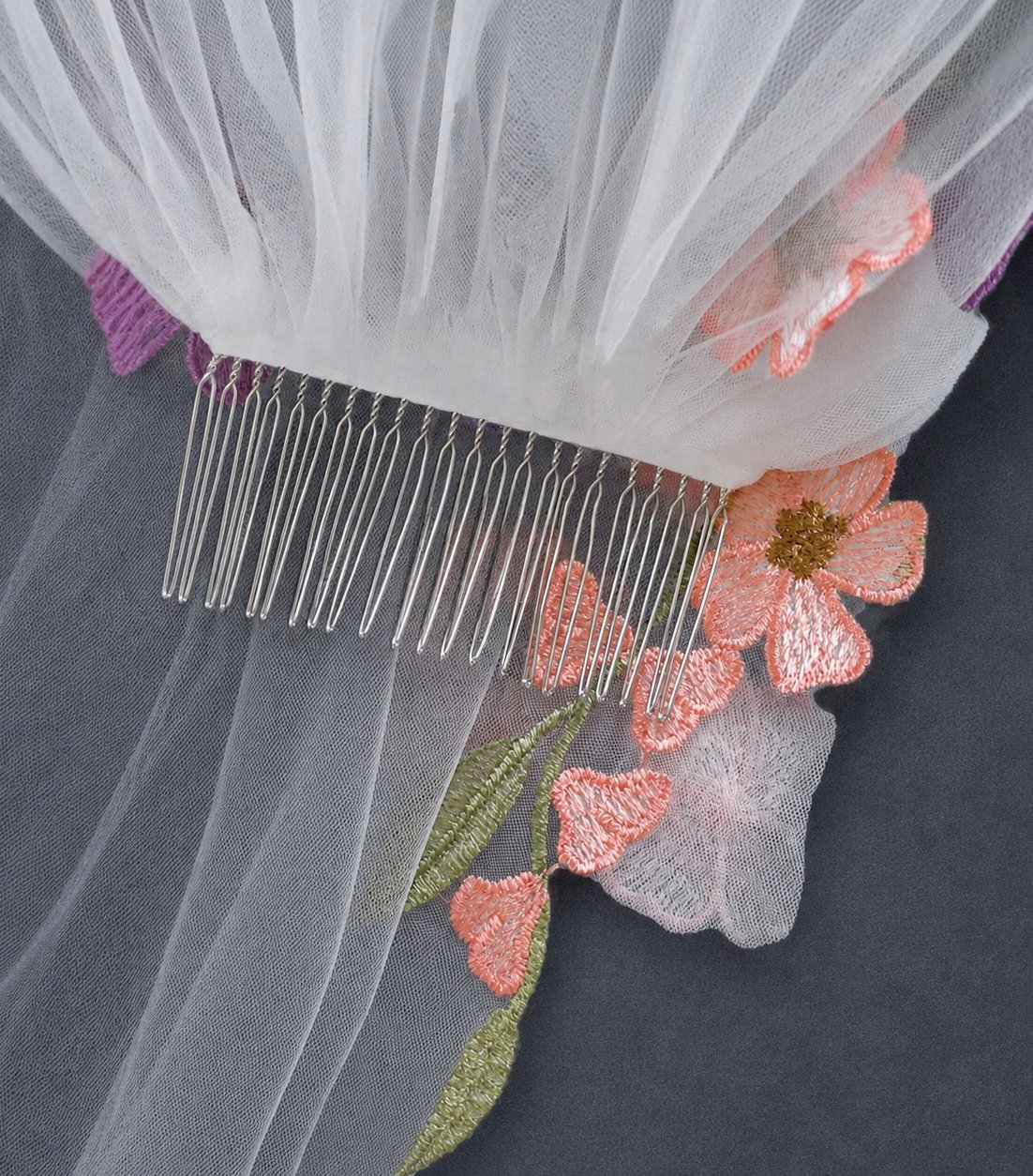 Metal bridal comb attached to light ivory tulle beside colorful embroidered flowers